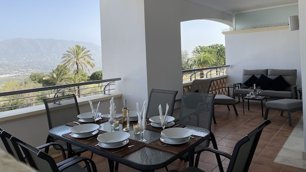 A dining area with a table set for four, overlooking a scenic view of mountains and palm trees. - Loasis, Luxueux et Calme 2 Chambres au Bord du Golf de la Cala, vue Montagnes (Mijas)