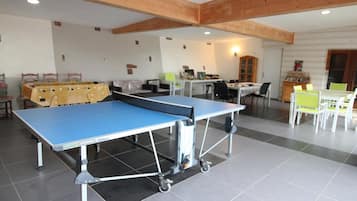 A spacious indoor area with a ping pong table, a foosball table, and a dining area with chairs and tables.
