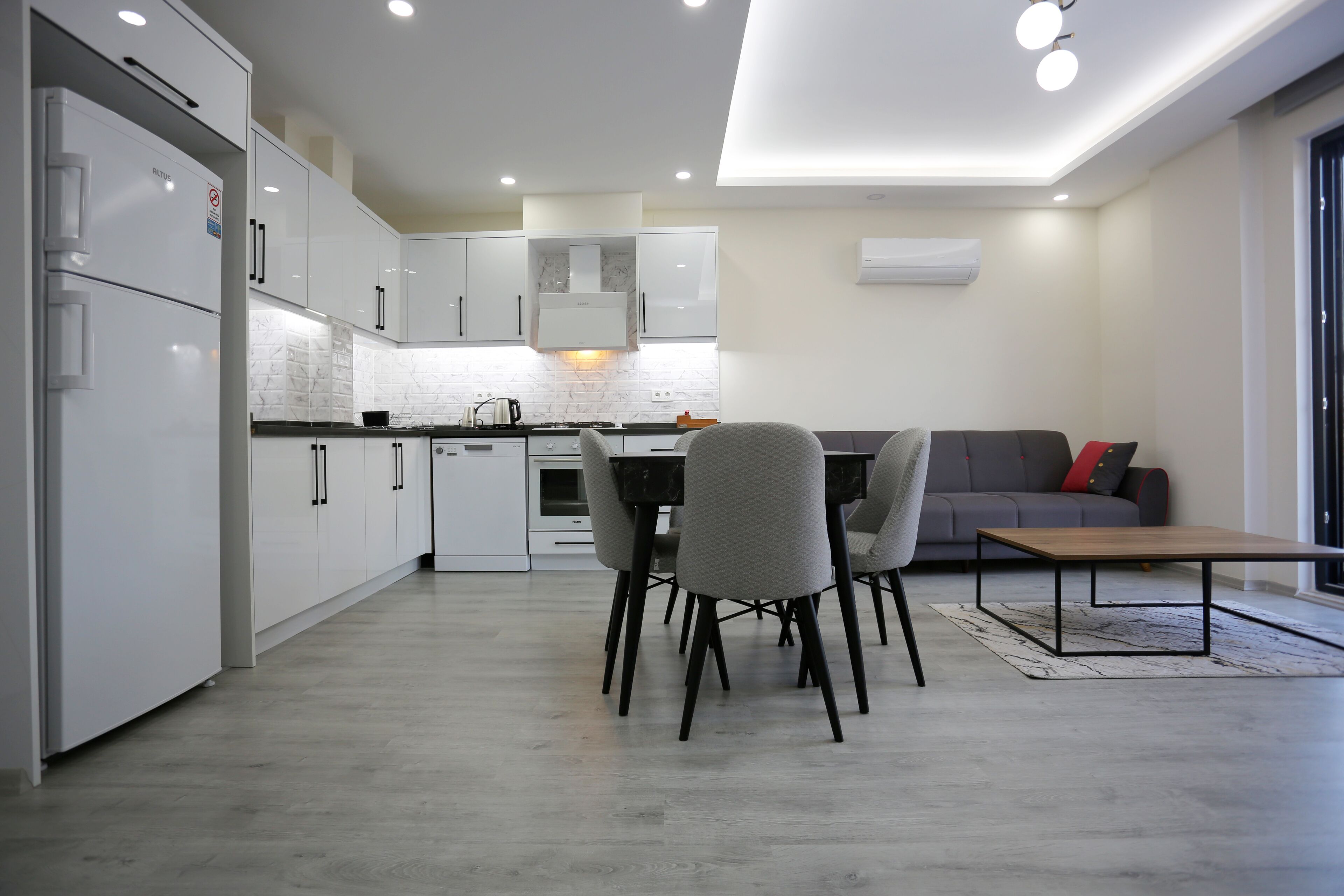 A modern kitchen with white cabinets, a dining area with chairs, a sofa, and a coffee table.