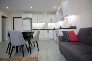 A modern kitchen with white cabinets, a dining table with chairs, and a gray sofa with red cushions. - Bright House Apart (Ortaca)