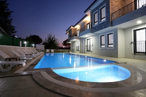 A swimming pool with lounge chairs and a building with balconies and windows. - Bright House Apart (Ortaca)