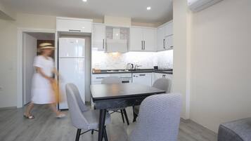 Une cuisine moderne avec des meubles blancs, un plan de travail noir et un coin repas avec des chaises grises.