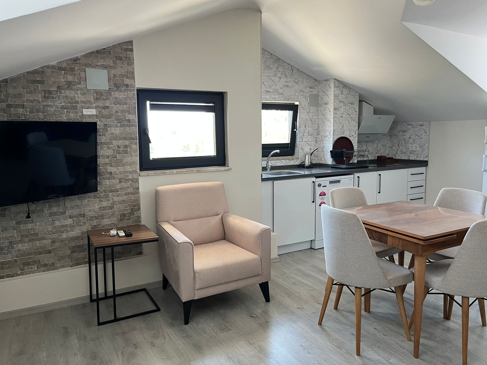 Un appartement moderne comprenant un coin repas, un salon avec télévision, une cuisine avec fenêtre et un mur en pierre.