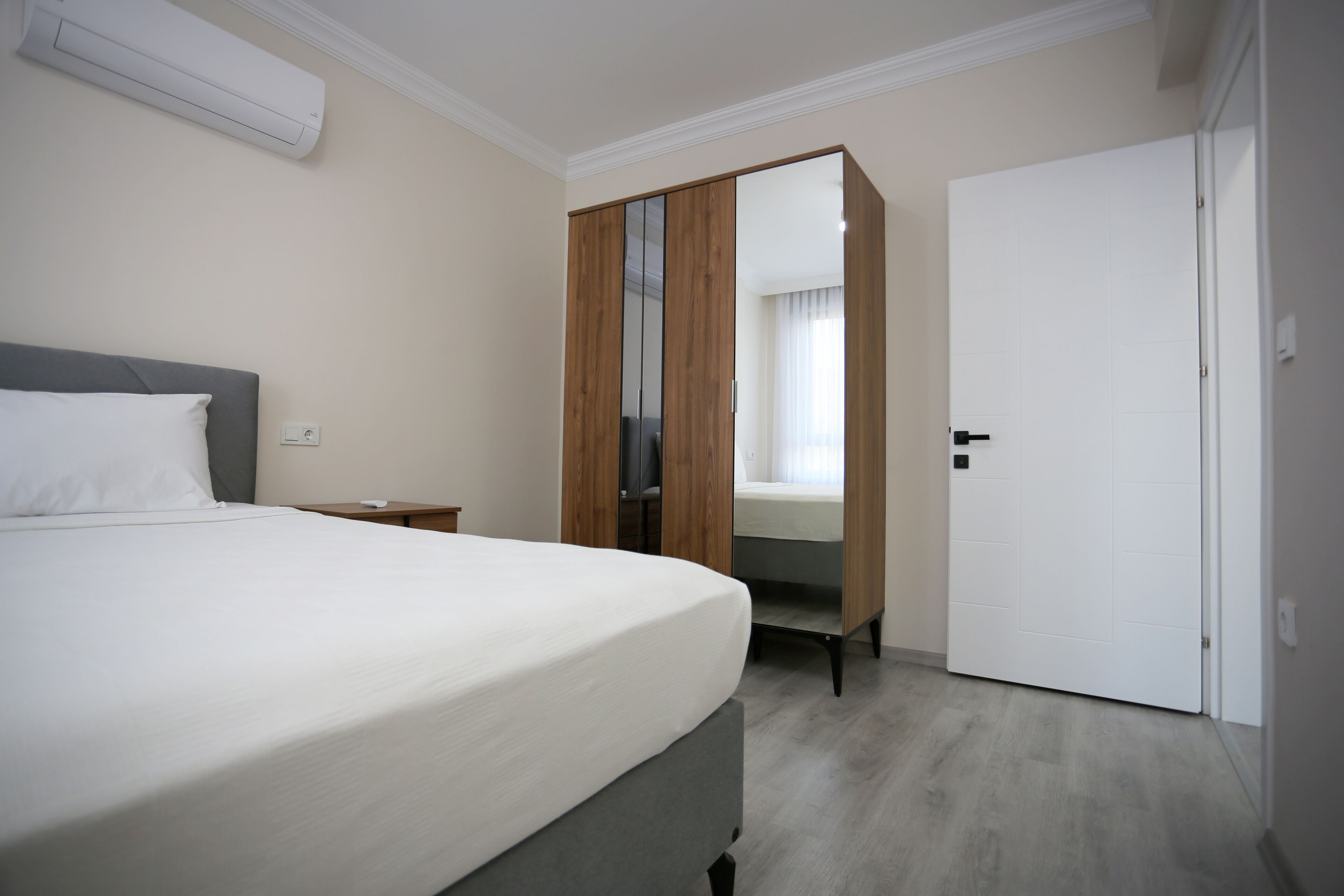Hotellihuone, jossa on sänky, vaatekaappi, ovi ja seinässä oleva valokytkin.