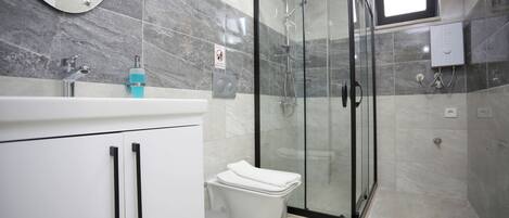 A modern bathroom with a glass-enclosed shower, a white sink with a blue soap dispenser, and a toilet.