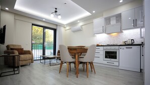 Une cuisine moderne avec des meubles blancs, un coin repas doté d’une table et de chaises en bois, et un canapé.