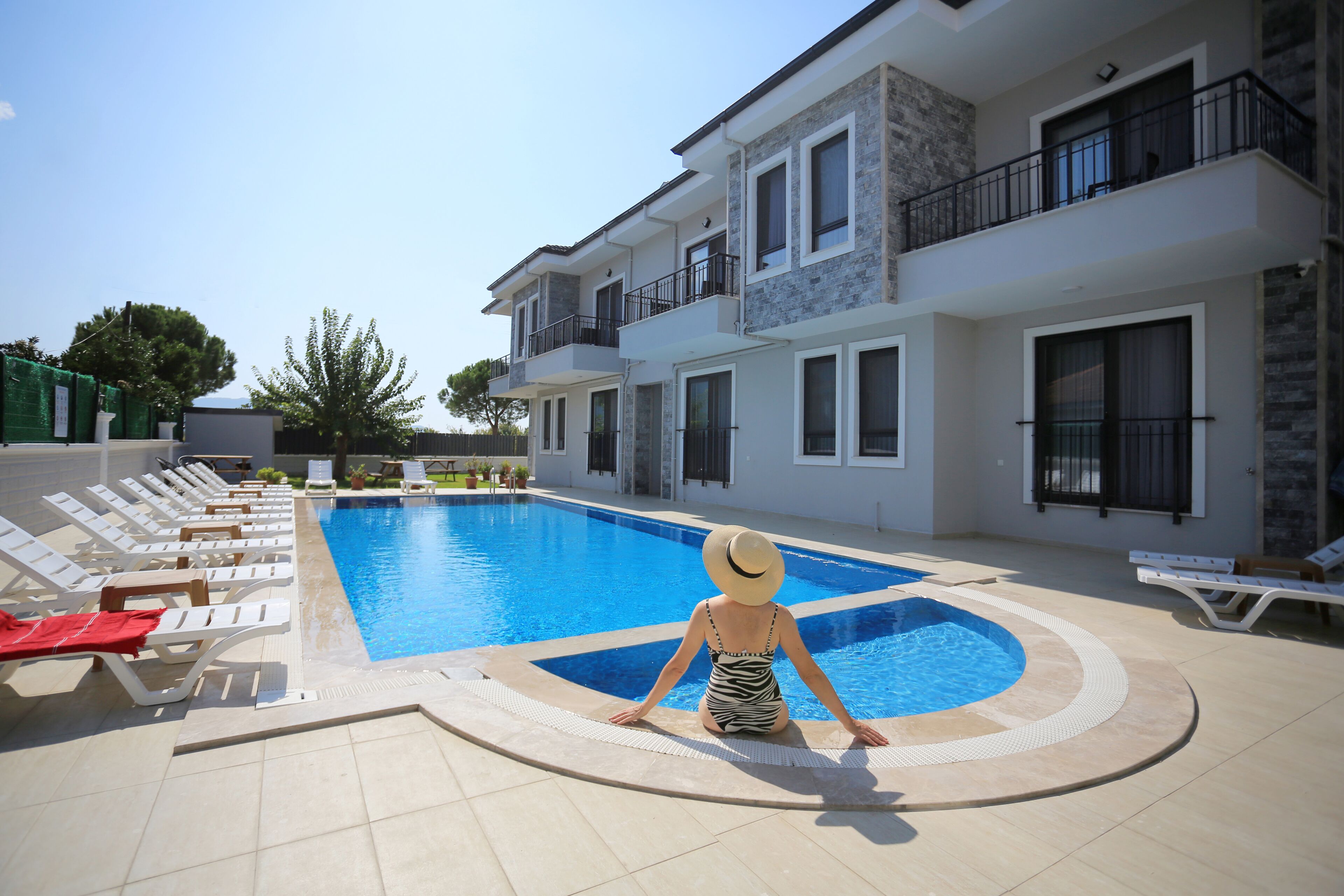 A swimming pool area with lounge chairs and a person sitting by the pool.