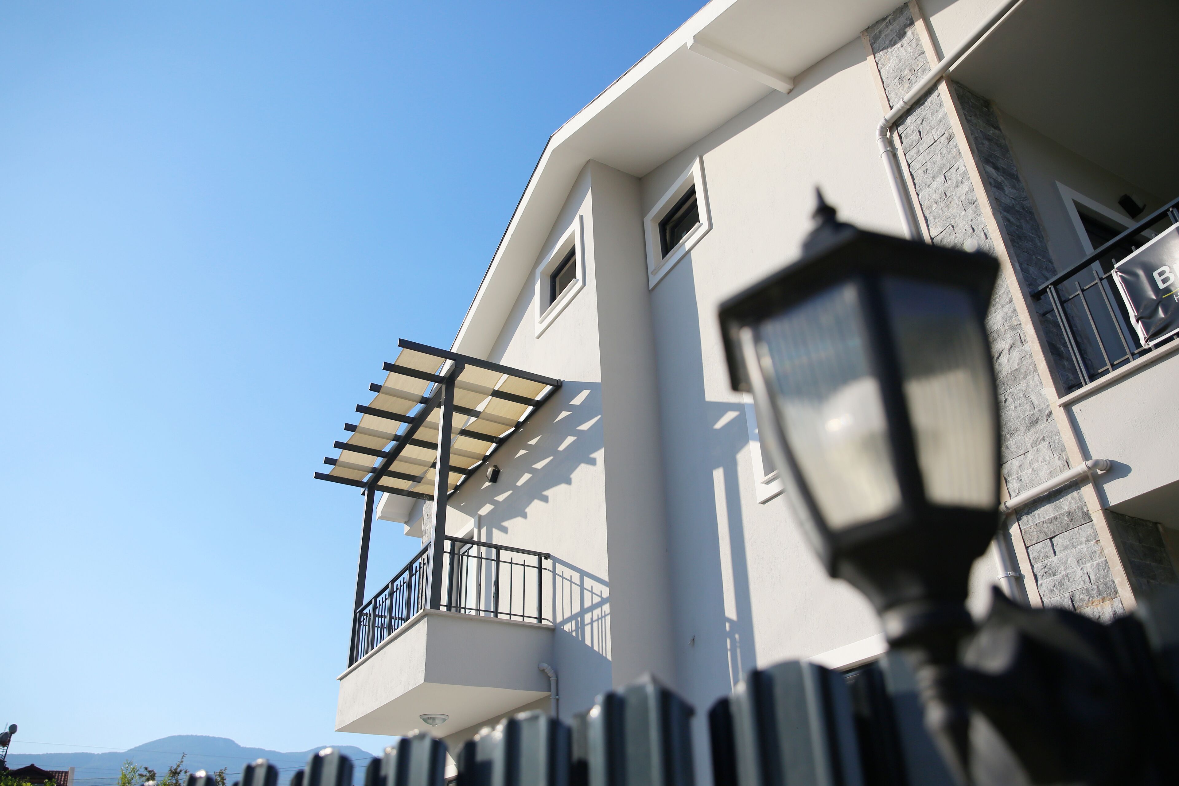 A modern building with a balcony, a pergola, and a street lamp.