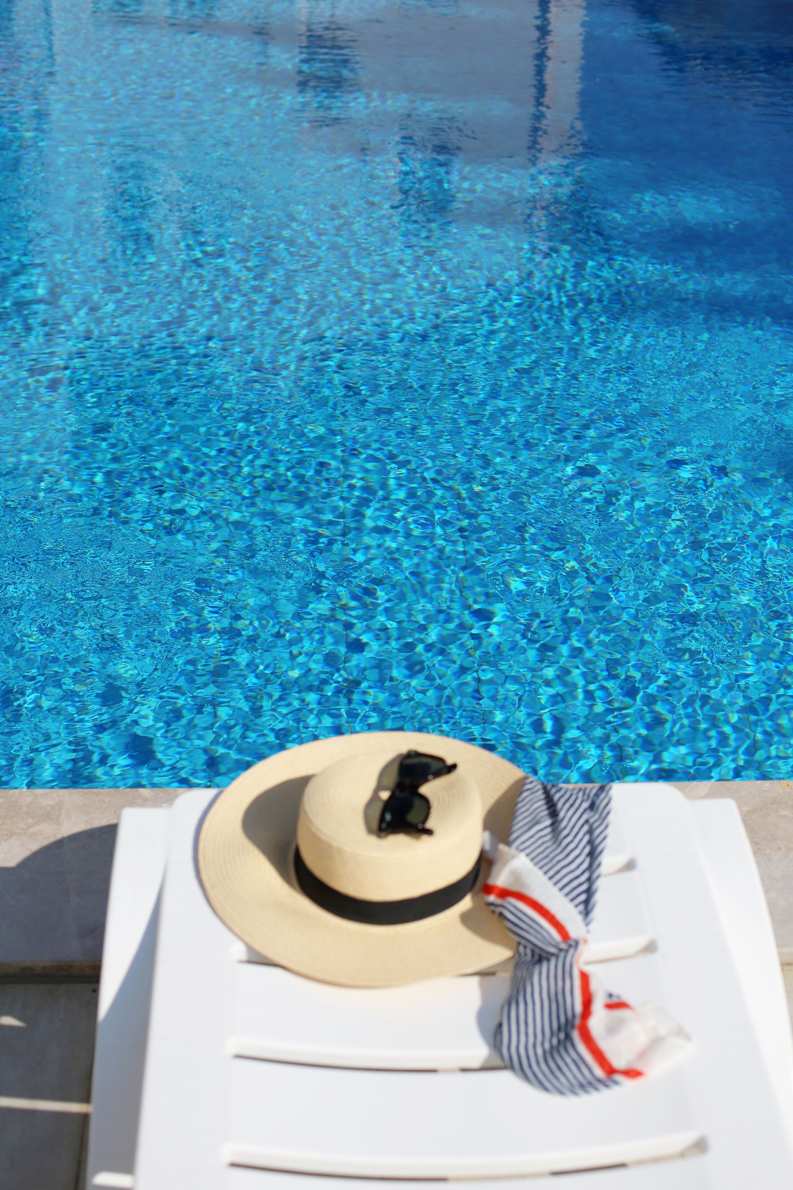 A poolside setting with a sun lounger, a hat, and a striped towel.