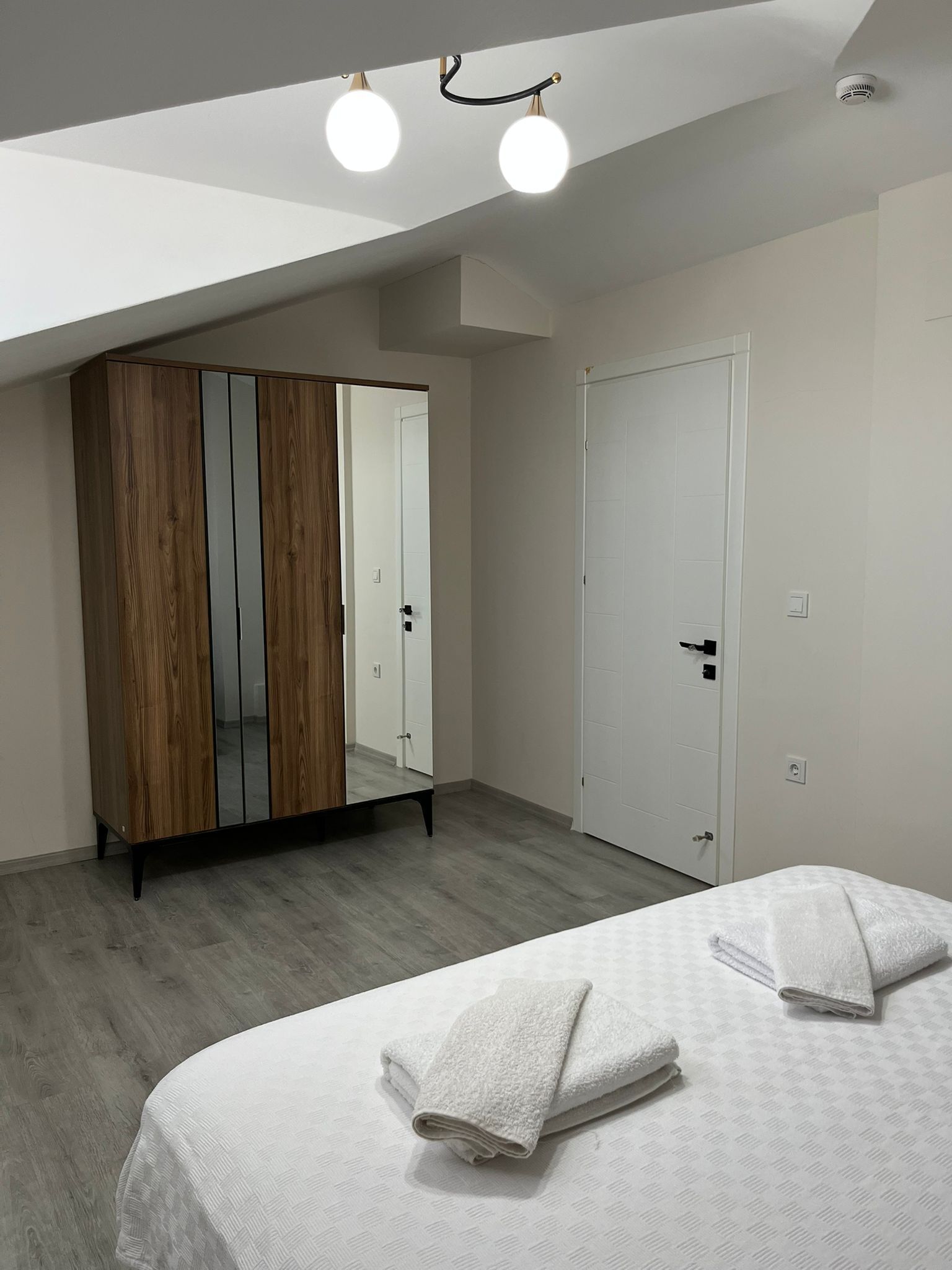 A bedroom with a wardrobe, a bed with towels, and a ceiling light fixture.