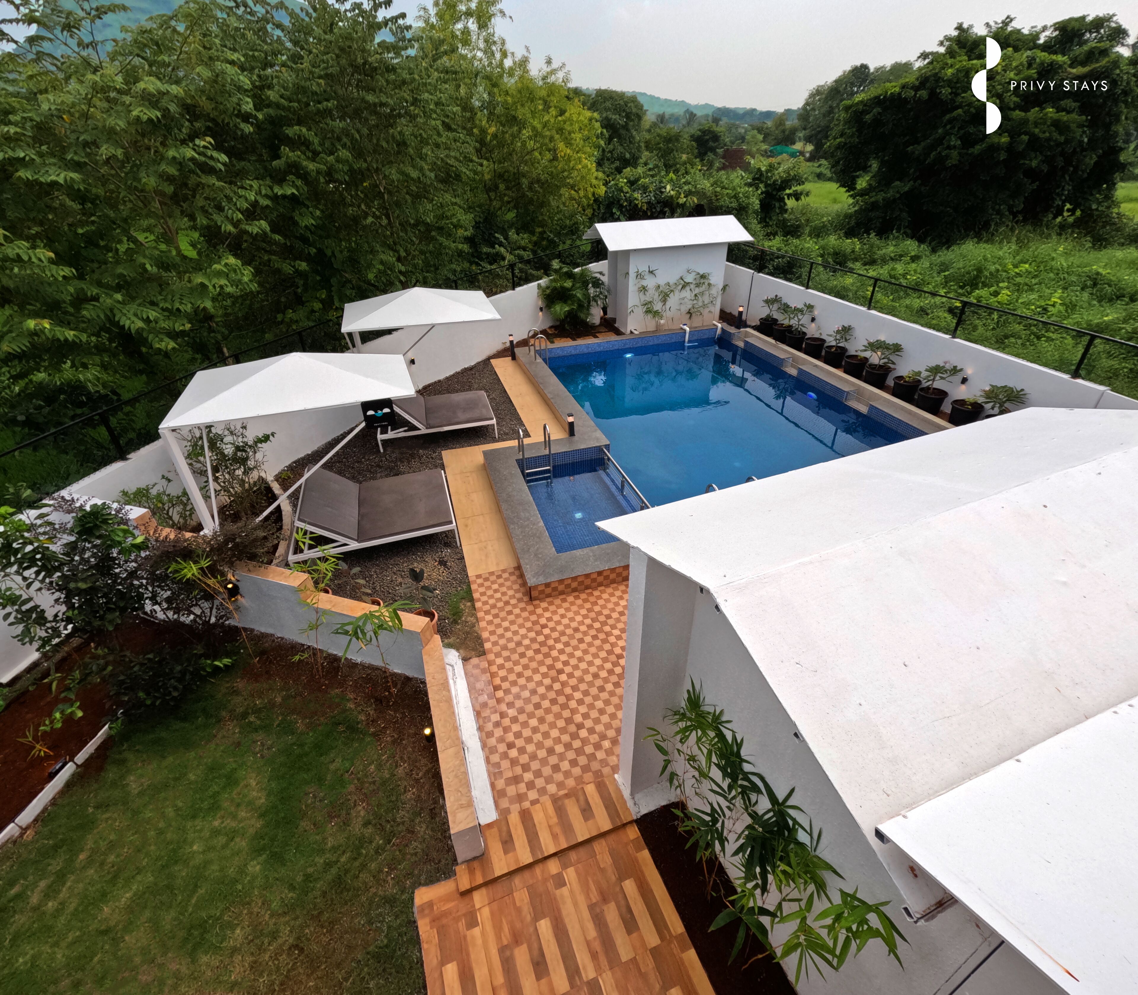 A rooftop pool area with lounge chairs and umbrellas, surrounded by greenery.