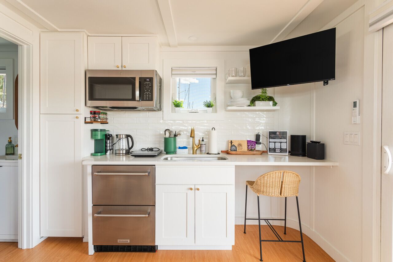 Una cocina moderna con armarios blancos, microondas integrado, cafetera y un taburete de bar.
