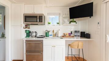 Una cocina moderna con armarios blancos, microondas integrado, cafetera y un taburete de bar.