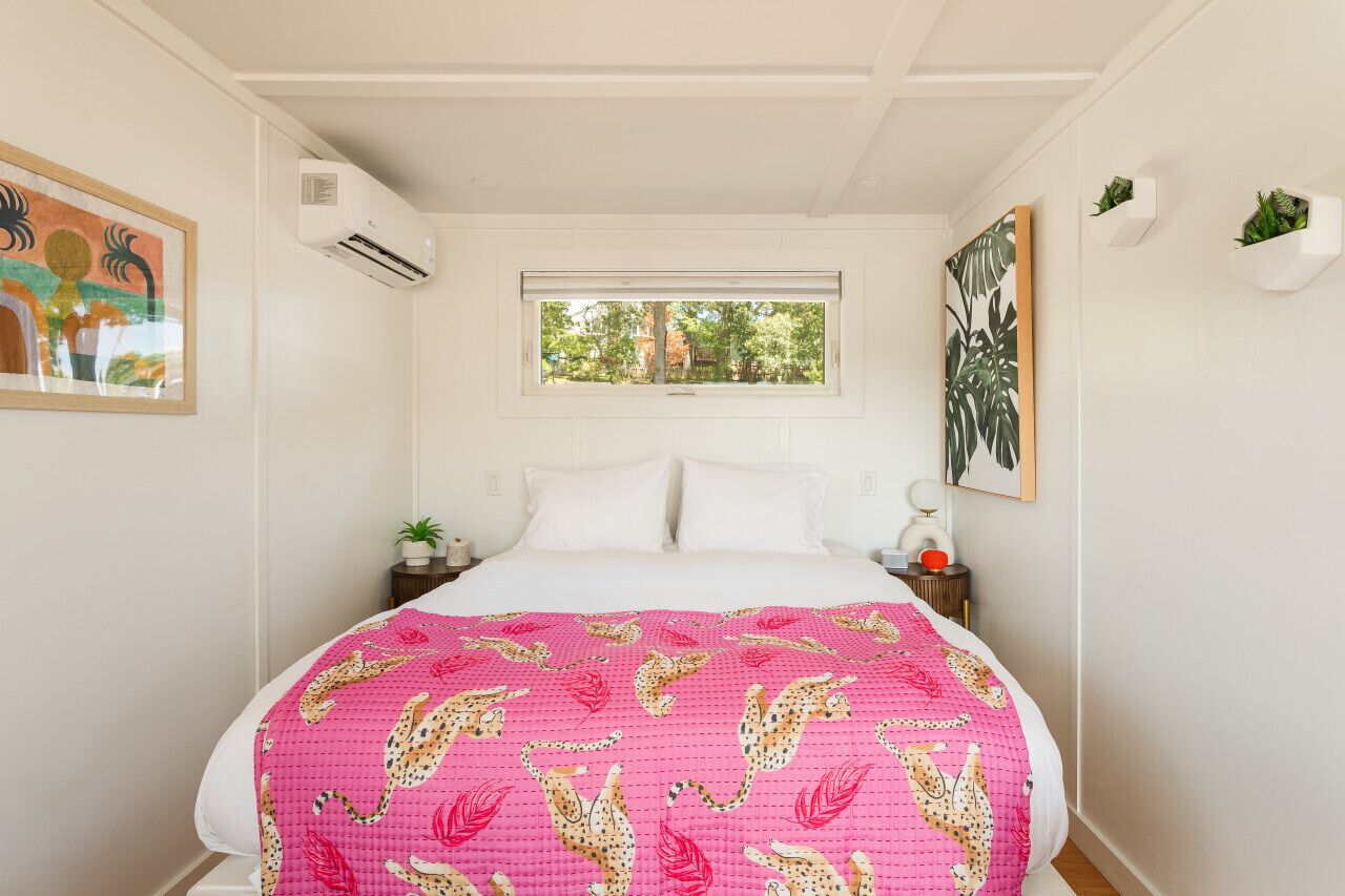 A bedroom with a bed, a window, a painting, and a wall-mounted air conditioner.