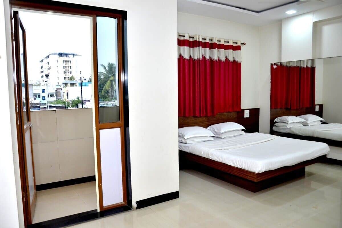 A hotel room with two beds, a balcony with a view of buildings, and red curtains.