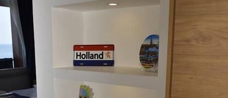 Habitación de hotel con pared blanca decorada con un cartel que dice 'Holland', una maqueta de molino y una pequeña figurita.