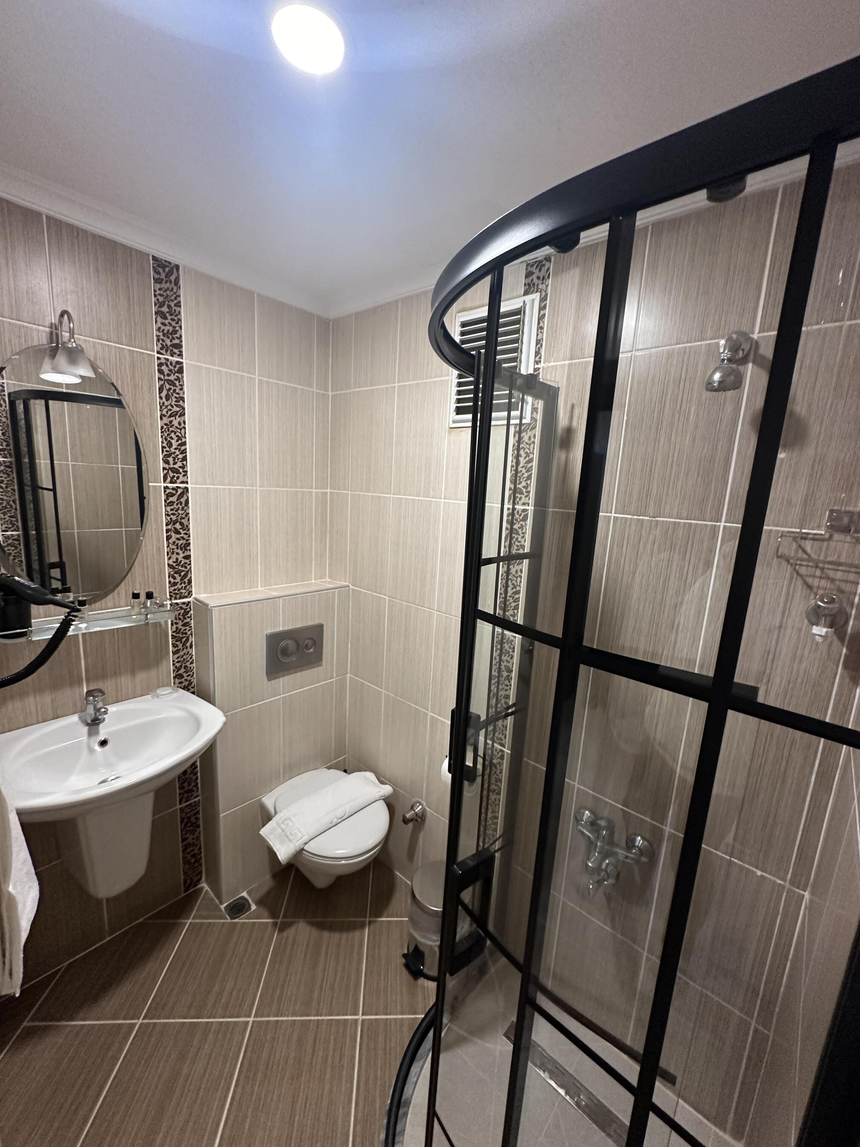 Un baño moderno con cabina de ducha de vidrio curvo, un lavabo con espejo y un inodoro.