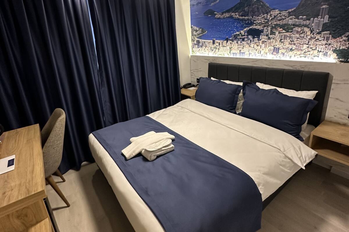 A hotel room with a bed, a desk, a chair, and a nightstand.