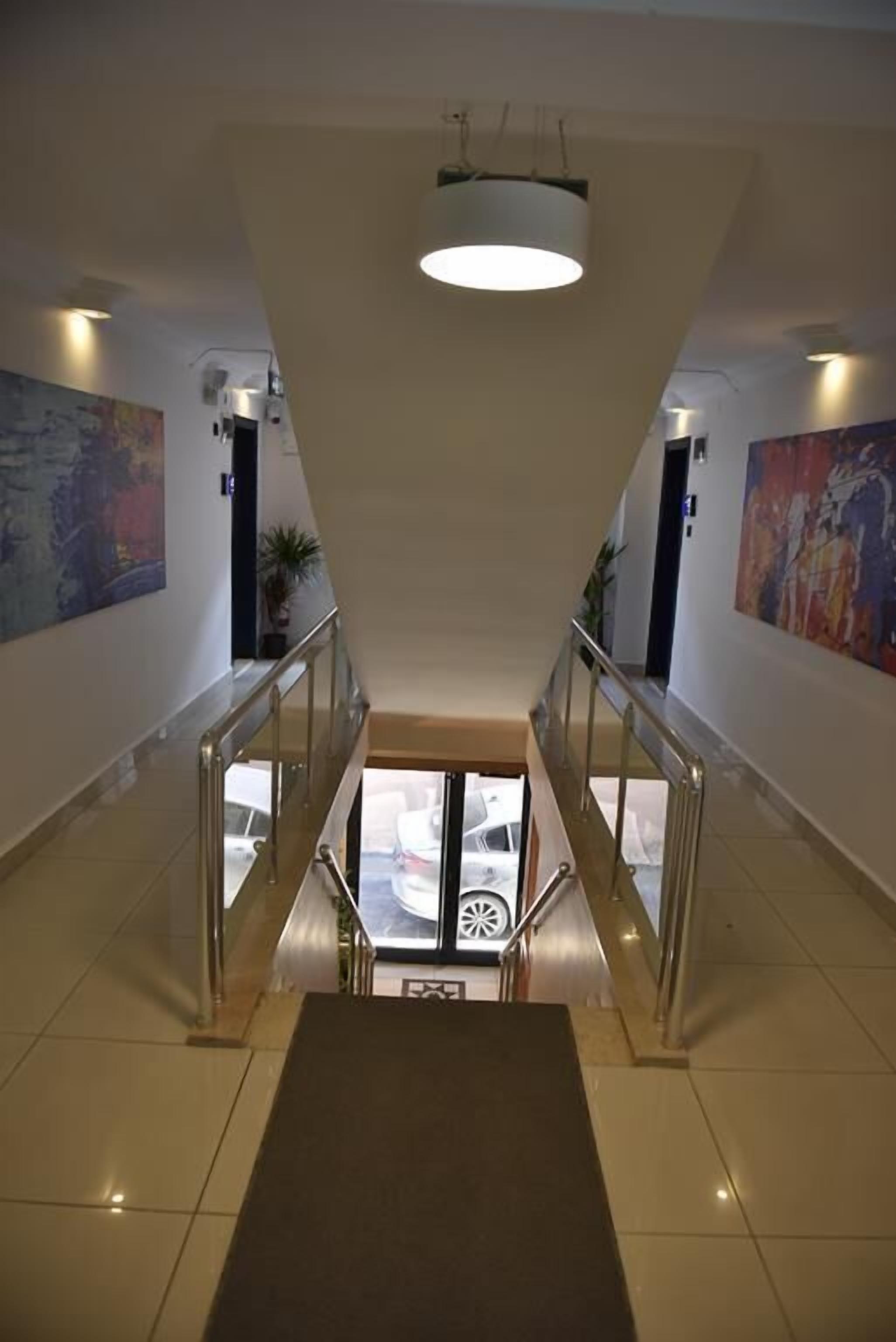Een moderne hotel lobby met een centrale trap, glazen deuren die naar een lager gelegen niveau leiden en kunstwerken aan de muren.