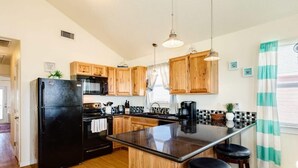 A modern kitchen with wooden cabinets, a black refrigerator, a central island with stools, and pendant lighting. - Ocean Pearl - Ultimate Beach & Boat Watch Escape! (Surfside Beach)