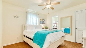 A bedroom with a bed, a ceiling fan, a window with curtains, a mirror, and a door. - Ocean Pearl - Ultimate Beach & Boat Watch Escape! (Surfside Beach)