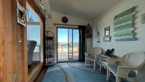A room with a view of the beach, a wicker chair, a small table, and a sign with cabin rules.