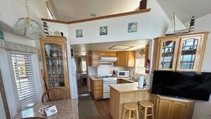 A compact kitchen with wooden cabinets, a microwave, a gas stove, and a flat-screen TV.