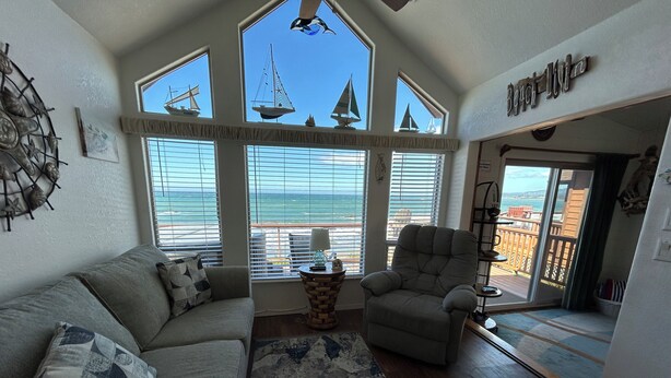 A spacious living area with a large window overlooking the sea, a cozy sofa, a comfortable armchair, and a small table with a lamp.