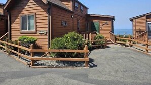 A wooden cabin-style building with a sloped roof, a front porch, and a view of the ocean.