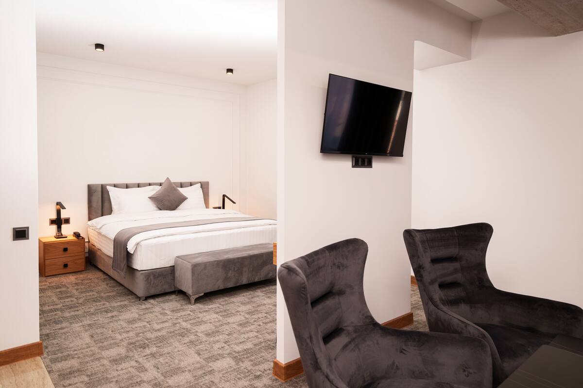 A bedroom with a bed, bedside table, lamp, and a TV mounted on the wall.