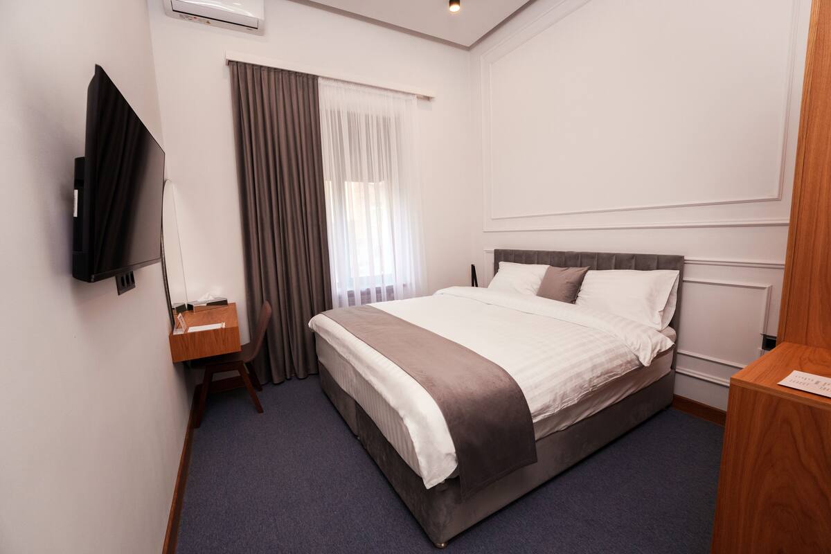 A hotel room with a bed, a desk, a television, and a window with curtains.