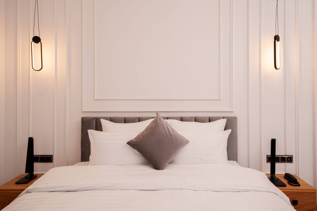 A neatly made bed with a grey headboard, two bedside tables with lamps, and a wall-mounted light fixture.