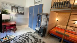 Una stanza compatta con un letto a castello, una scrivania con una sedia, un tavolino, un tappeto decorativo e un condizionatore d'aria a parete.