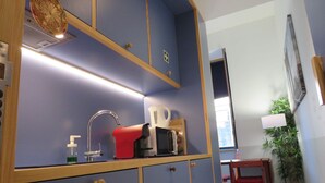 Una camera compatta con una parete blu, un mobiletto in legno con cassetti, una sedia rossa, un tavolino e una pianta in vaso.