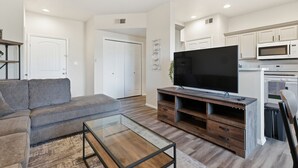 A modern living room with a grey sofa, a glass coffee table, and a TV on a wooden stand. - Renovated 3BR with Yard & Mountain Views (Rio Rancho)