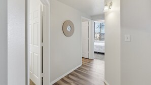 A hallway with a wooden floor, white walls, and a round mirror on the wall. - Renovated 3BR with Yard & Mountain Views (Rio Rancho)