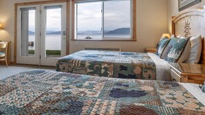 Ein Schlafzimmer mit zwei Betten, einem großen Fenster mit Meerblick und einem Holzkopfende.
