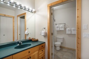 Bany amb un moble de tocador de fusta, un lavabo i un mirall amb il·luminació. Hi ha un vàter i un suport de tovalloles amb tovalloles.