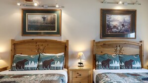 A double room with two wooden beds, each with a headboard, a bedside table, and a lamp. There are two framed pictures on the wall above the beds. - Lakefront Studio with views! (Bigfork)