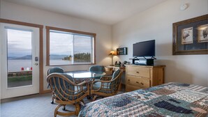 A bedroom with a bed, a desk, two chairs, a TV, a lamp, and a window with a view of the outdoors. - New! Waterfront Studio near Glacier! (Bigfork)
