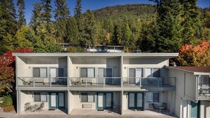 A two-story building with balconies, outdoor seating, and a view of a forested hillside. - New! Waterfront Studio near Glacier! (Bigfork)