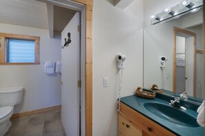 Een badkamer met een wit toilet, een houten wastafelmeubel met een groene wasbak en een spiegel met verlichting erboven.