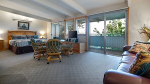 A bedroom with a large bed, two chairs, a desk, and a sofa. There is a sliding glass door leading to a balcony.
