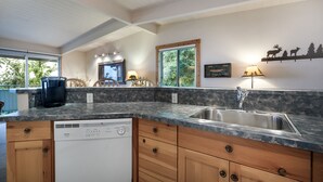 A modern kitchen with a built-in dishwasher, wooden cabinets, a granite countertop, a stainless steel sink, and a window overlooking greenery.