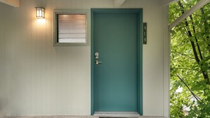 A teal door with a window above it and a small light fixture to the left.