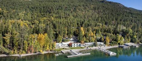 Una proprietà sul lago con un molo, un edificio grande e una collina boscosa sullo sfondo.