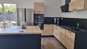 A modern kitchen with wooden cabinets, a black countertop, and a built-in oven. - House in Piriac Sur Mer ideal for spending time with family or friends. (Piriac-sur-Mer)