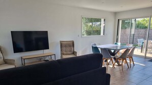 A modern living room with a flat-screen TV, a sofa, a dining table with chairs, and a sliding glass door leading to an outdoor area. - House in Piriac Sur Mer ideal for spending time with family or friends. (Piriac-sur-Mer)