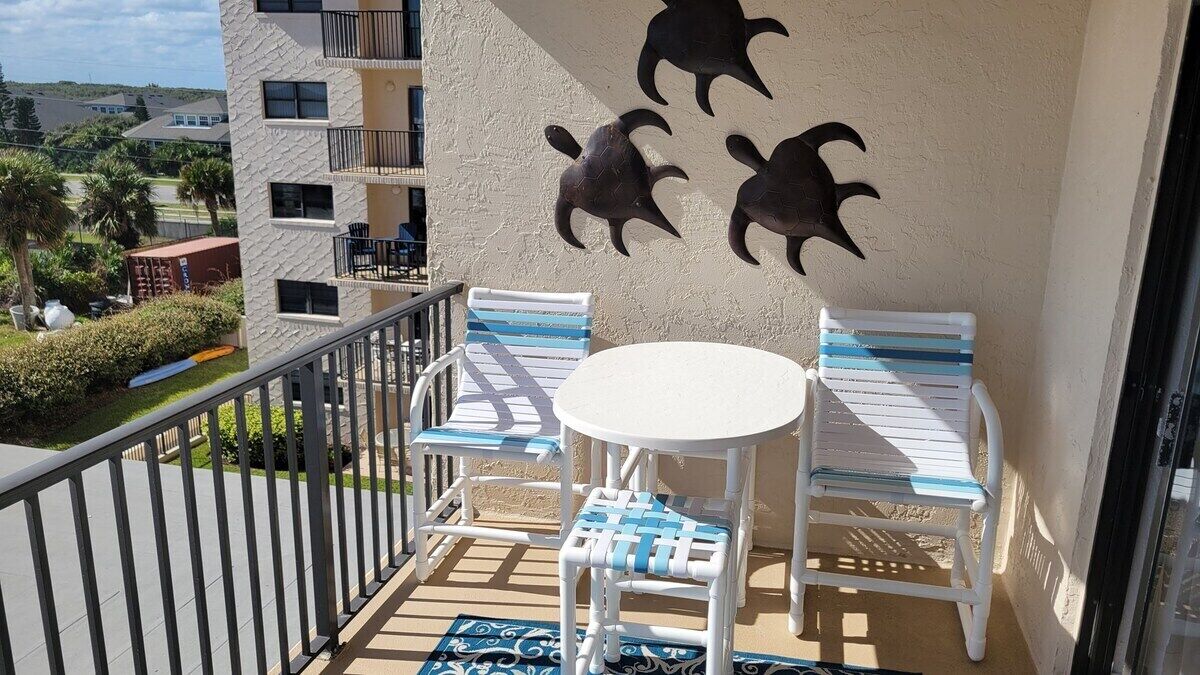 Un balcone con un tavolo rotondo e due sedie, un muro decorativo con sculture di tartarughe marine e vista sul paesaggio circostante.