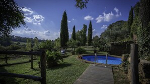 Eine Holzterrasse führt zu einem Schwimmbecken, das von Grünpflanzen und hohen Bäumen umgeben ist.